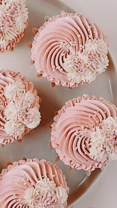 four cupcakes with pink frosting and white flowers on top sitting on a plate