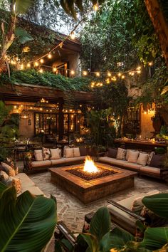 a fire pit in the middle of a patio surrounded by greenery and hanging lights