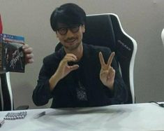 a man sitting at a table with two fingers up in front of him and the peace sign