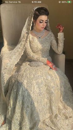 a woman sitting in a chair wearing a wedding dress and holding her hand up to her face