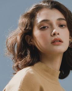 a woman with brown hair wearing a tan turtle neck sweater and gold hoop earrings looking off to the side