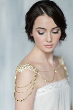 a woman wearing a white dress with gold chains on her arm and necklace around her shoulder