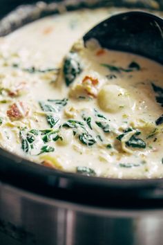 a pot filled with cheese and spinach on top of a stove next to a ladle