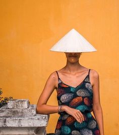 a woman with a hat on her head standing in front of a yellow wall