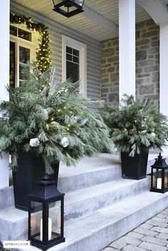 two black planters with pine cones on the front steps next to lanterns and christmas lights