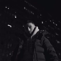 a man standing in front of a tall building at night with his hands on his hips