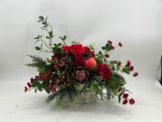 a bouquet of red flowers and greenery in a silver vase on a white background