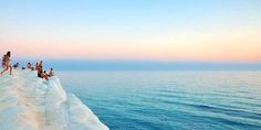 people are standing on the edge of an ice - covered cliff overlooking the ocean at sunset