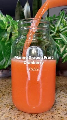 an orange juice is being poured into a mason jar with the words mango dragon fruit cranberry juice