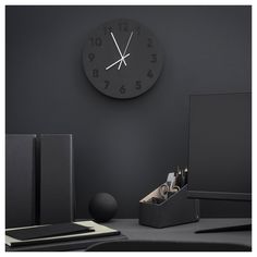 a black clock on the wall above a desk with a computer and other office supplies