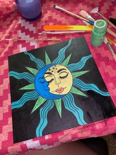 the sun and moon is painted on a pink tablecloth with other paints, pencils, and markers