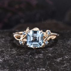 an aqua blue topazte and diamond ring sits on a black surface, surrounded by stones