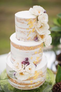 a three tiered cake with flowers on top and pine cones in the back ground