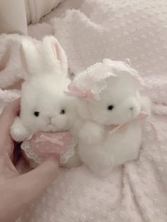 two stuffed animals sitting on top of a bed next to someone's hand holding one