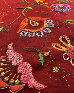 closeup of an embroidered fabric with flowers and birds on it, in bright colors