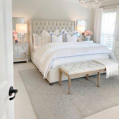 a large white bed sitting in a bedroom next to a window with a chandelier