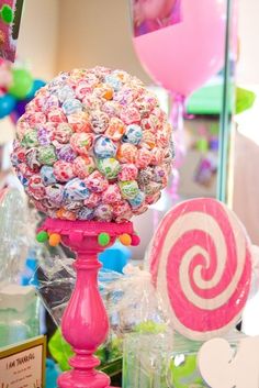 there is a large candy ball on top of a stand next to some lollipops