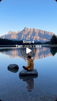 a person sitting on top of a rock next to a lake