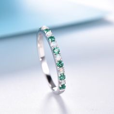 a white gold ring with green and white stones on the side, sitting on a table