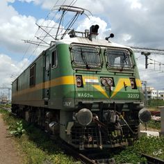 a green and yellow train traveling down tracks next to power lines on a cloudy day