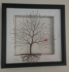 a red bird sitting on top of a tree branch in a white wooden frame with black trim