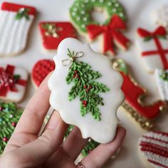 a hand holding a decorated christmas cookie in front of other cookies on a white surface