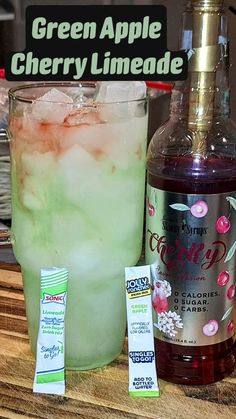 a bottle of green apple cherry limeade next to a glass filled with ice and liquid