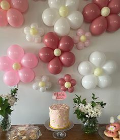 a table topped with a cake covered in pink and white balloons next to other desserts