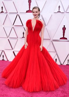 a woman in a red gown standing on the pink carpet at an oscars event