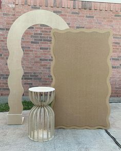 there is a small table with a vase next to it on the sidewalk near a brick wall