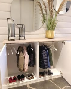 a white shelf with shoes and plants on it in front of a mirror that is hanging from the wall