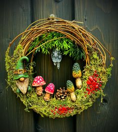 a wreath with gnomes and mushrooms is hanging on a wooden door, surrounded by greenery