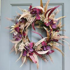 a wreath is hanging on the door with purple flowers and greenery in front of it