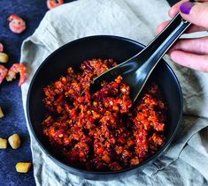 a person holding a spoon in a bowl filled with chili and corn kernels on the side