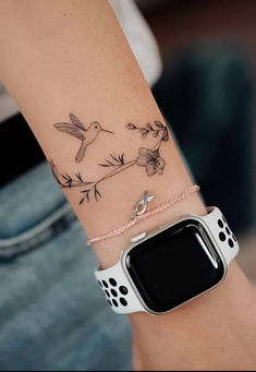 a woman's arm with a bird and flower tattoo on it, while she is wearing an apple watch