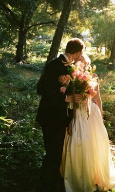 a bride and groom kissing in the woods with sun shining through the trees behind them