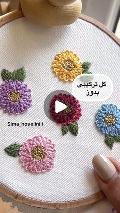 a hand is holding a cross stitch project with flowers on it and the words in arabic