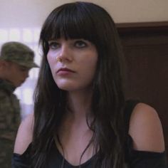 a woman with long black hair and blue eyes is looking off to the side while another man in uniform stands behind her