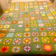 a green crocheted blanket with multicolored flowers on it sitting on top of a bed