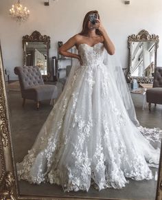 a woman taking a selfie in front of a mirror wearing a white wedding dress