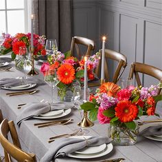 a table set with place settings, candles and flowers in vases on the tables