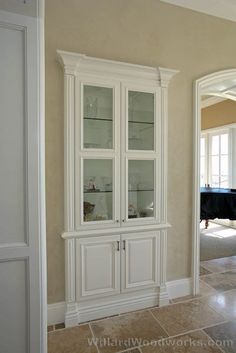 a white china cabinet with glass doors in the middle of a room next to a black piano