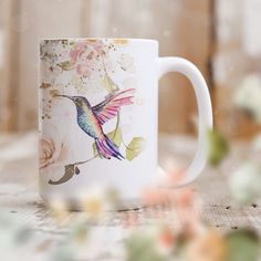 a white coffee mug with a colorful hummingbird on it's side sitting on a table