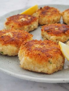 some crab cakes with lemon wedges on a white and gray plate, ready to be eaten