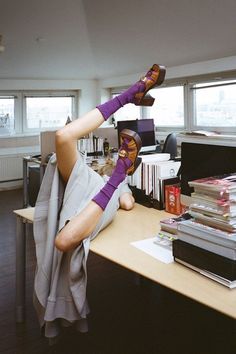 a woman in purple socks laying on top of a desk next to a pile of books