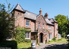 an old brick building with lots of windows on the front and side, surrounded by greenery