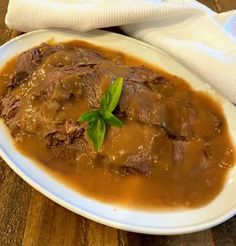 a white plate topped with meat and gravy on top of a wooden table