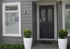 two large white planters in front of a gray house with black door and windows