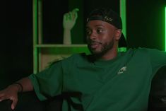 a man in a green shirt sitting on a black chair with his arms crossed and looking at the camera