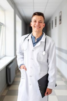 a male doctor in a white coat is smiling and holding a black folder while standing on a checkered floor